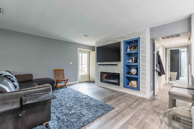 living room featuring built in features, light hardwood / wood-style floors, and a premium fireplace