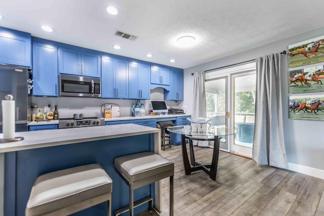 kitchen featuring hardwood / wood-style flooring, blue cabinetry, stainless steel appliances, a kitchen bar, and a textured ceiling