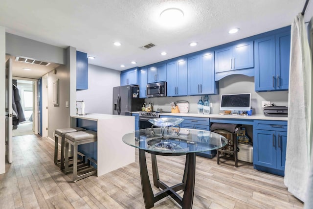 kitchen featuring blue cabinetry, appliances with stainless steel finishes, light hardwood / wood-style floors, a breakfast bar area, and a textured ceiling