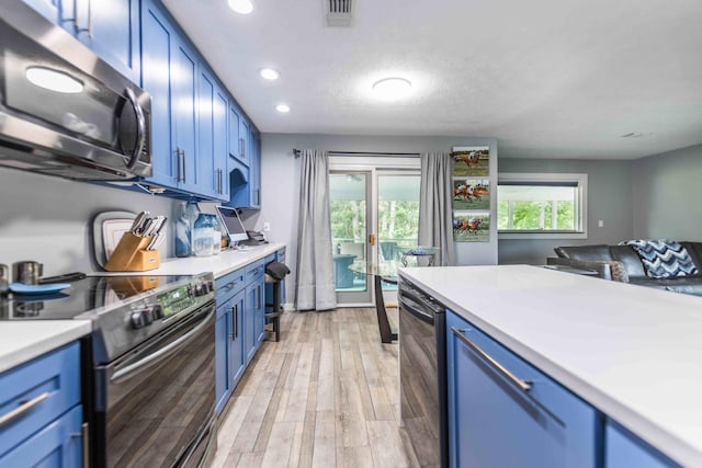 kitchen with blue cabinets, appliances with stainless steel finishes, a textured ceiling, and light wood-type flooring