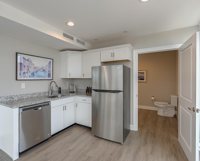 kitchen featuring light stone counters, stainless steel appliances, sink, light hardwood / wood-style floors, and white cabinetry