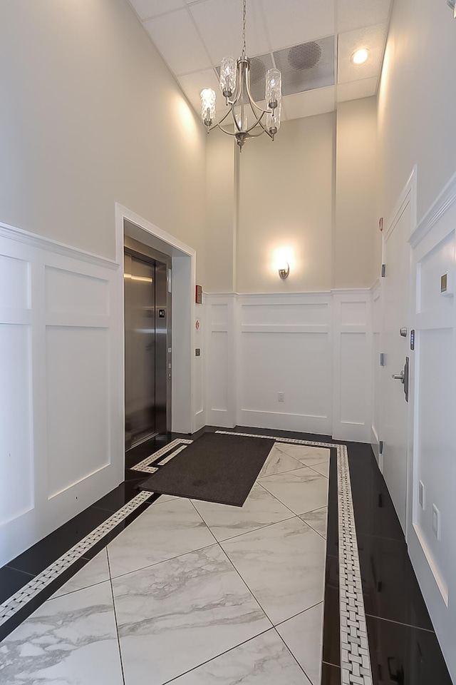 doorway featuring elevator, a towering ceiling, and a chandelier