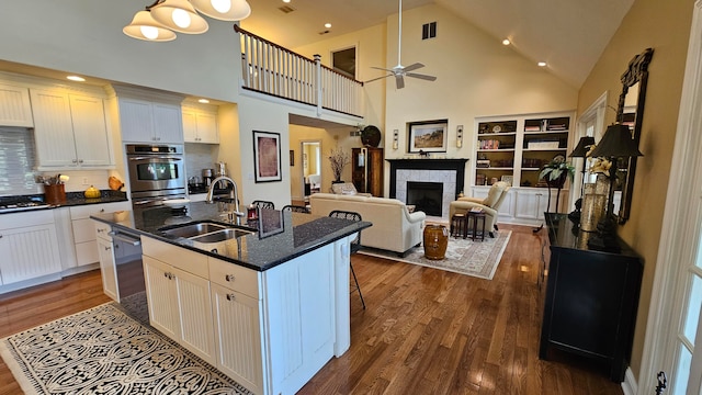 kitchen featuring a fireplace, a kitchen island with sink, high vaulted ceiling, sink, and ceiling fan