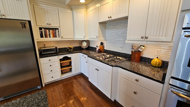 kitchen with appliances with stainless steel finishes, dark hardwood / wood-style flooring, white cabinetry, dark stone counters, and tasteful backsplash