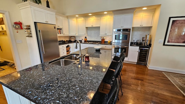 kitchen featuring backsplash, stainless steel appliances, dark hardwood / wood-style flooring, beverage cooler, and a kitchen island with sink