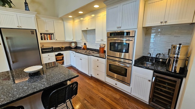 kitchen featuring beverage cooler, backsplash, appliances with stainless steel finishes, dark wood-type flooring, and dark stone counters