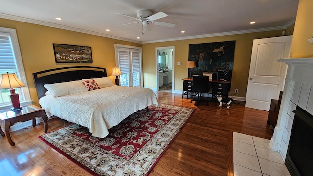 bedroom with a tile fireplace, hardwood / wood-style flooring, ensuite bath, ceiling fan, and ornamental molding