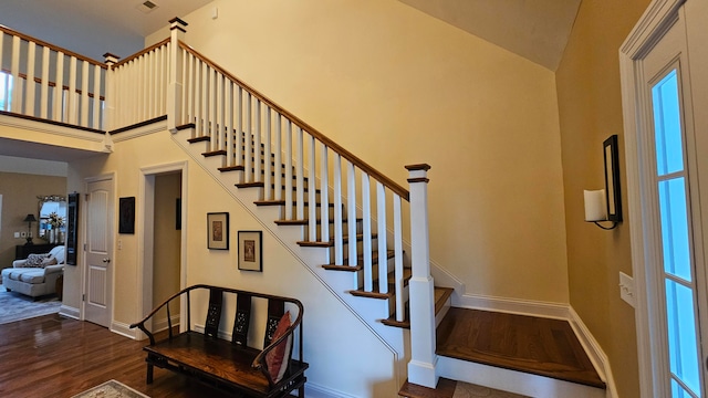 stairway with wood-type flooring and a towering ceiling