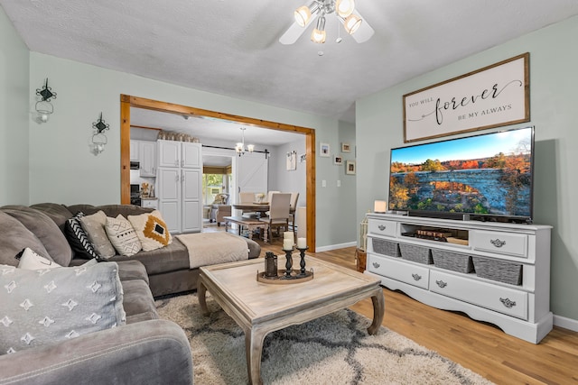 living room featuring ceiling fan with notable chandelier, light hardwood / wood-style floors, and a textured ceiling