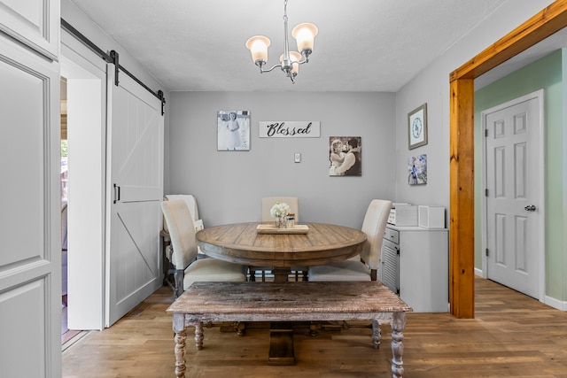 dining area with a textured ceiling, a barn door, light wood-type flooring, and a chandelier