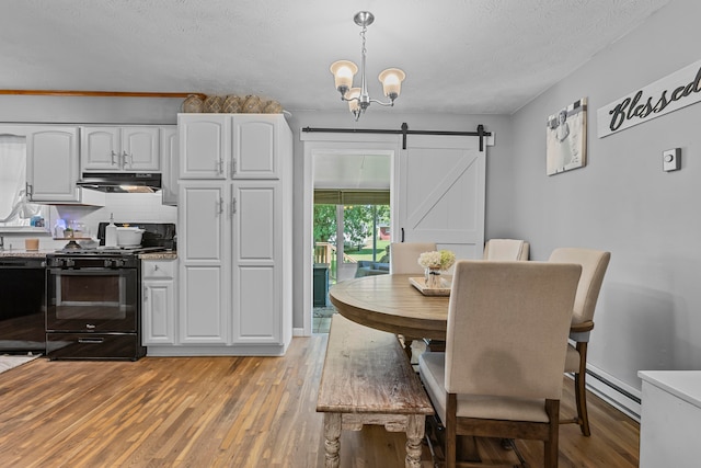 dining space featuring a barn door, a baseboard heating unit, light wood-type flooring, a notable chandelier, and a textured ceiling