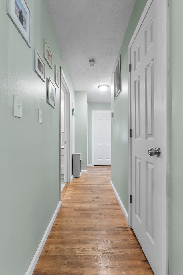 hall with a textured ceiling and light hardwood / wood-style floors