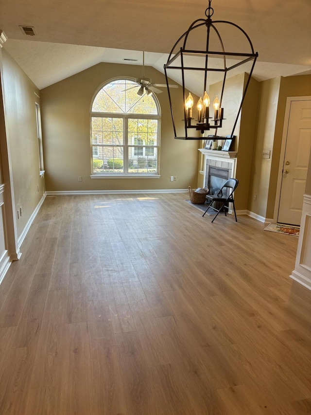 empty room featuring wood finished floors, visible vents, lofted ceiling, a fireplace, and ceiling fan with notable chandelier