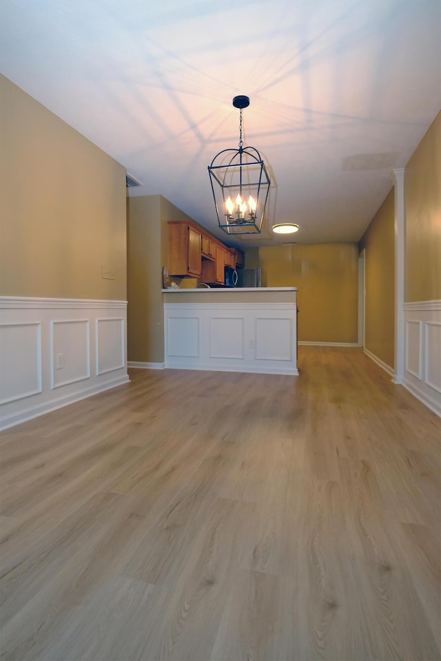 unfurnished living room featuring a notable chandelier, light wood-style flooring, and a decorative wall