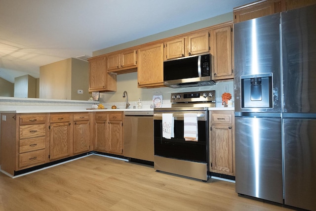 kitchen featuring stainless steel appliances, light wood-style floors, a peninsula, and light countertops