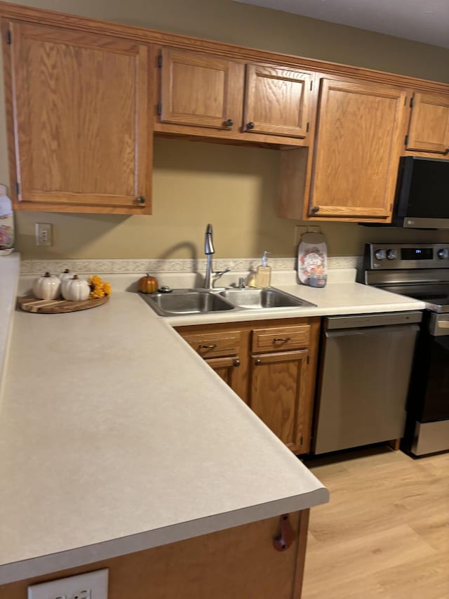 kitchen featuring brown cabinetry, stainless steel appliances, a sink, light countertops, and light wood-style floors