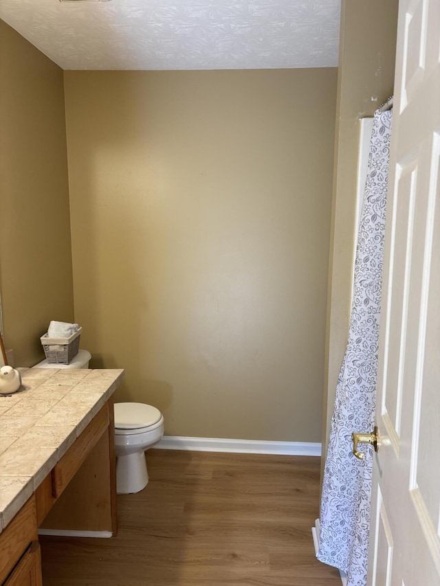 bathroom with toilet, a textured ceiling, wood finished floors, baseboards, and vanity