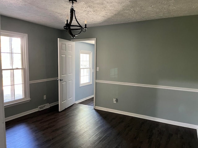 empty room with plenty of natural light, dark hardwood / wood-style flooring, and a textured ceiling