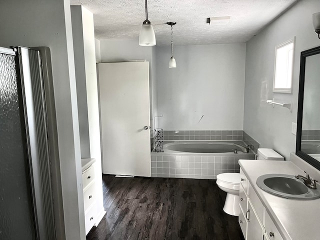 bathroom with a textured ceiling, vanity, hardwood / wood-style floors, toilet, and tiled tub