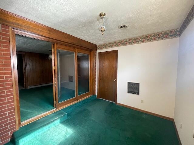 carpeted spare room featuring a baseboard heating unit and a textured ceiling