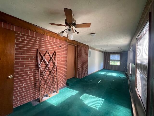 carpeted empty room with a textured ceiling, brick wall, and ceiling fan