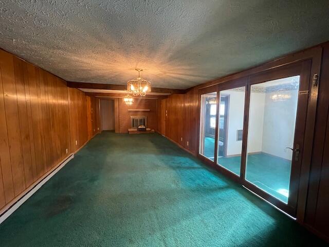 spare room with a textured ceiling, a large fireplace, dark carpet, and an inviting chandelier