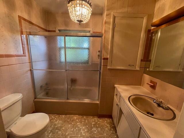 full bathroom with toilet, tile patterned flooring, vanity, bath / shower combo with glass door, and tile walls