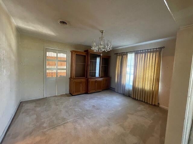 unfurnished dining area with ornamental molding, a chandelier, and carpet floors