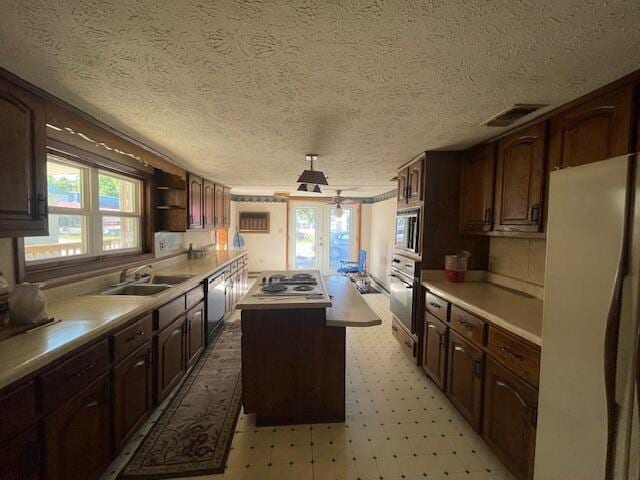 kitchen with a textured ceiling, stainless steel appliances, a center island, sink, and dark brown cabinetry