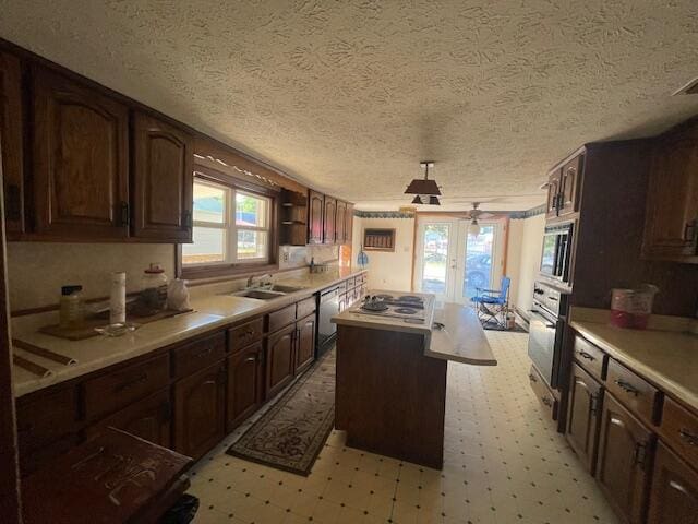 kitchen with a textured ceiling, dark brown cabinets, appliances with stainless steel finishes, a center island, and sink