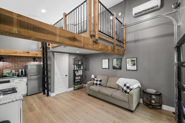 living room featuring a wall mounted AC, a towering ceiling, and light wood-type flooring