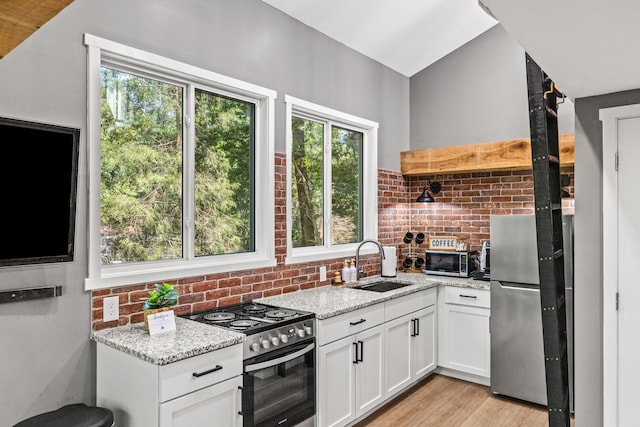 kitchen with light hardwood / wood-style flooring, appliances with stainless steel finishes, sink, light stone counters, and white cabinets