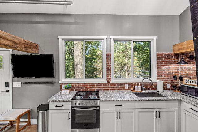 kitchen featuring light stone counters, sink, white cabinets, and electric range