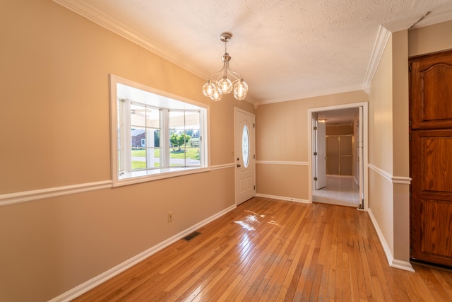 unfurnished room featuring light wood-type flooring, ornamental molding, a notable chandelier, and a textured ceiling