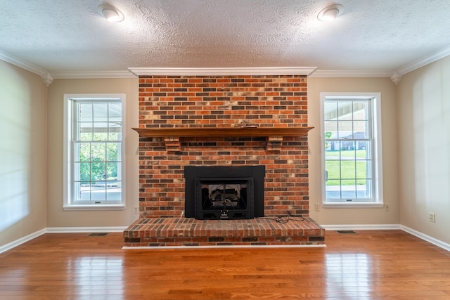 unfurnished living room with a textured ceiling, plenty of natural light, wood-type flooring, and a brick fireplace