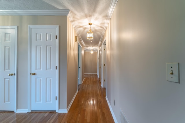 hall with a textured ceiling, ornamental molding, and hardwood / wood-style flooring