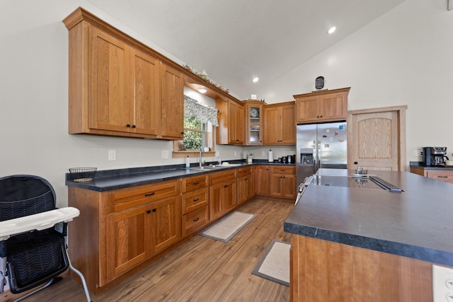 kitchen with dark countertops, glass insert cabinets, a sink, light wood-type flooring, and stainless steel fridge with ice dispenser