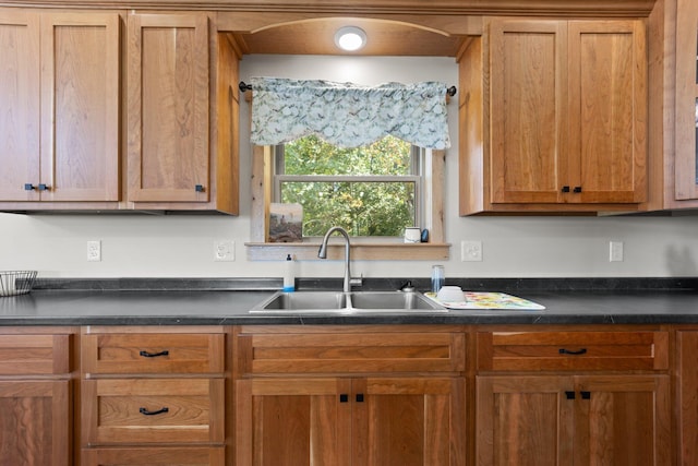 kitchen with brown cabinetry, dark countertops, and a sink