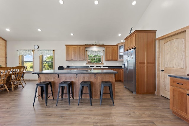 kitchen featuring stainless steel fridge with ice dispenser, dark countertops, a kitchen breakfast bar, brown cabinets, and a kitchen island with sink