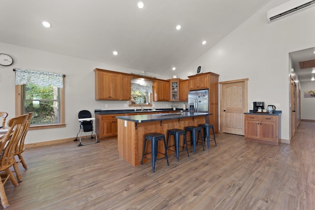 kitchen with brown cabinetry, stainless steel fridge with ice dispenser, dark countertops, glass insert cabinets, and a wall mounted AC