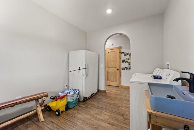 washroom with arched walkways, wood finished floors, a sink, separate washer and dryer, and laundry area