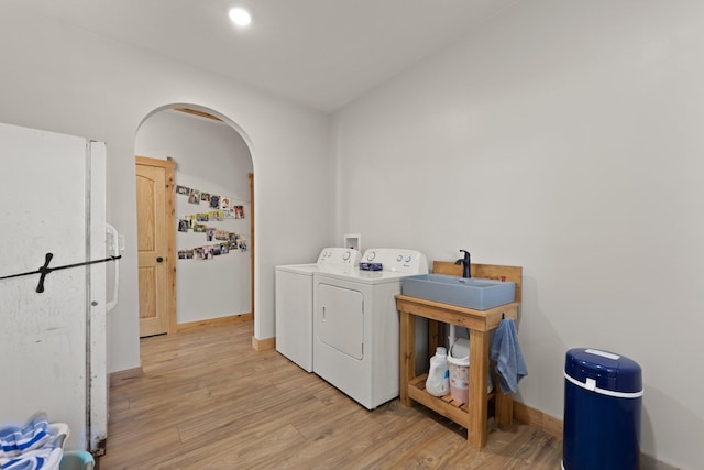 laundry area with laundry area, light wood finished floors, arched walkways, independent washer and dryer, and a sink