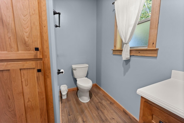 half bath with toilet, baseboards, and wood finished floors