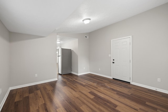 spare room with a textured ceiling, vaulted ceiling, and dark hardwood / wood-style floors