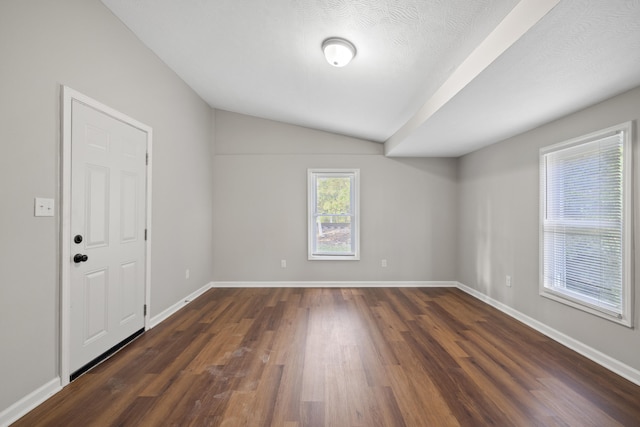 spare room with dark wood-type flooring, vaulted ceiling, and a textured ceiling