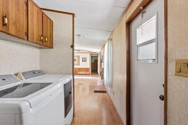 laundry room with washing machine and dryer, cabinets, wood walls, and light wood-type flooring