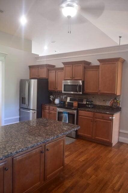 kitchen featuring appliances with stainless steel finishes, dark wood-type flooring, decorative backsplash, ceiling fan, and dark stone counters