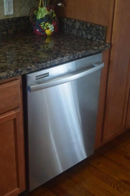 room details featuring dark hardwood / wood-style floors, dark stone counters, and stainless steel dishwasher