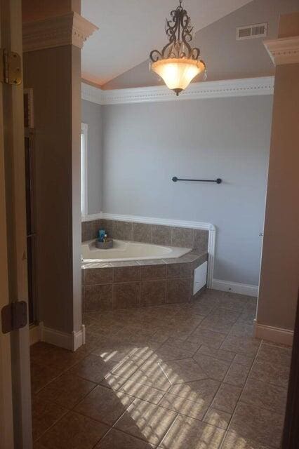 bathroom with crown molding, vaulted ceiling, a relaxing tiled tub, and tile patterned floors