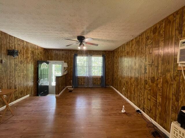 spare room with a textured ceiling, ceiling fan, wood walls, and dark hardwood / wood-style flooring